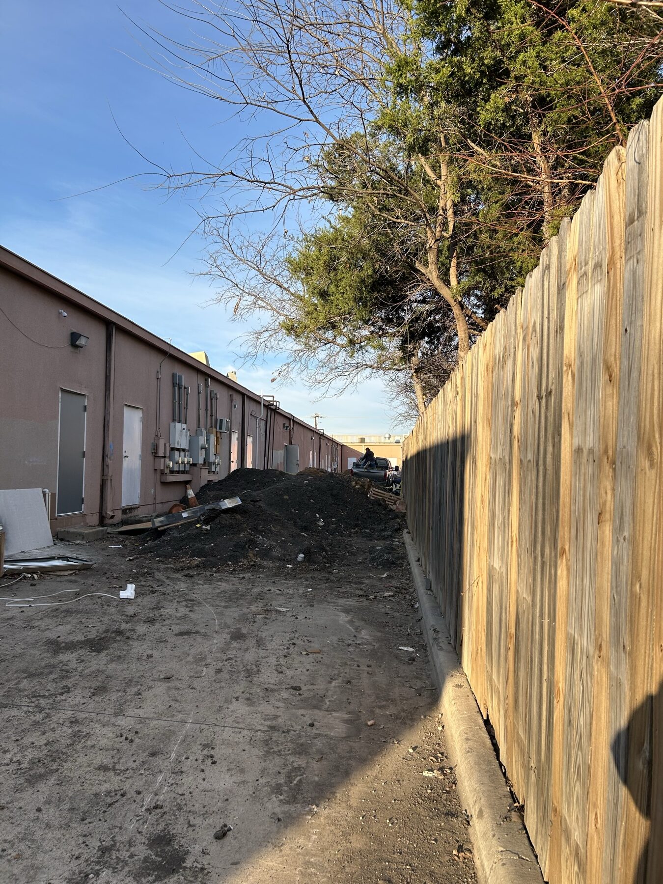 Excavated soil staged behind the center — customer parking untouched