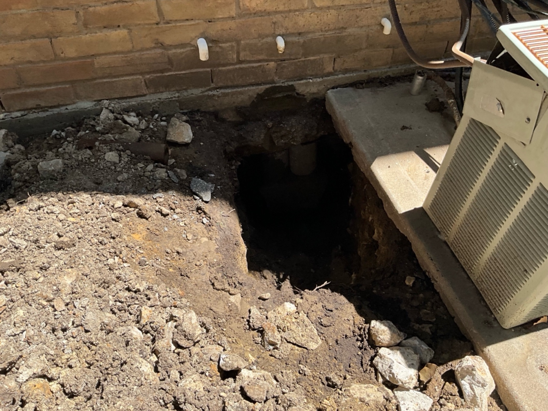An access hole opened beside the slab, spoil kept clear of lawns and walks