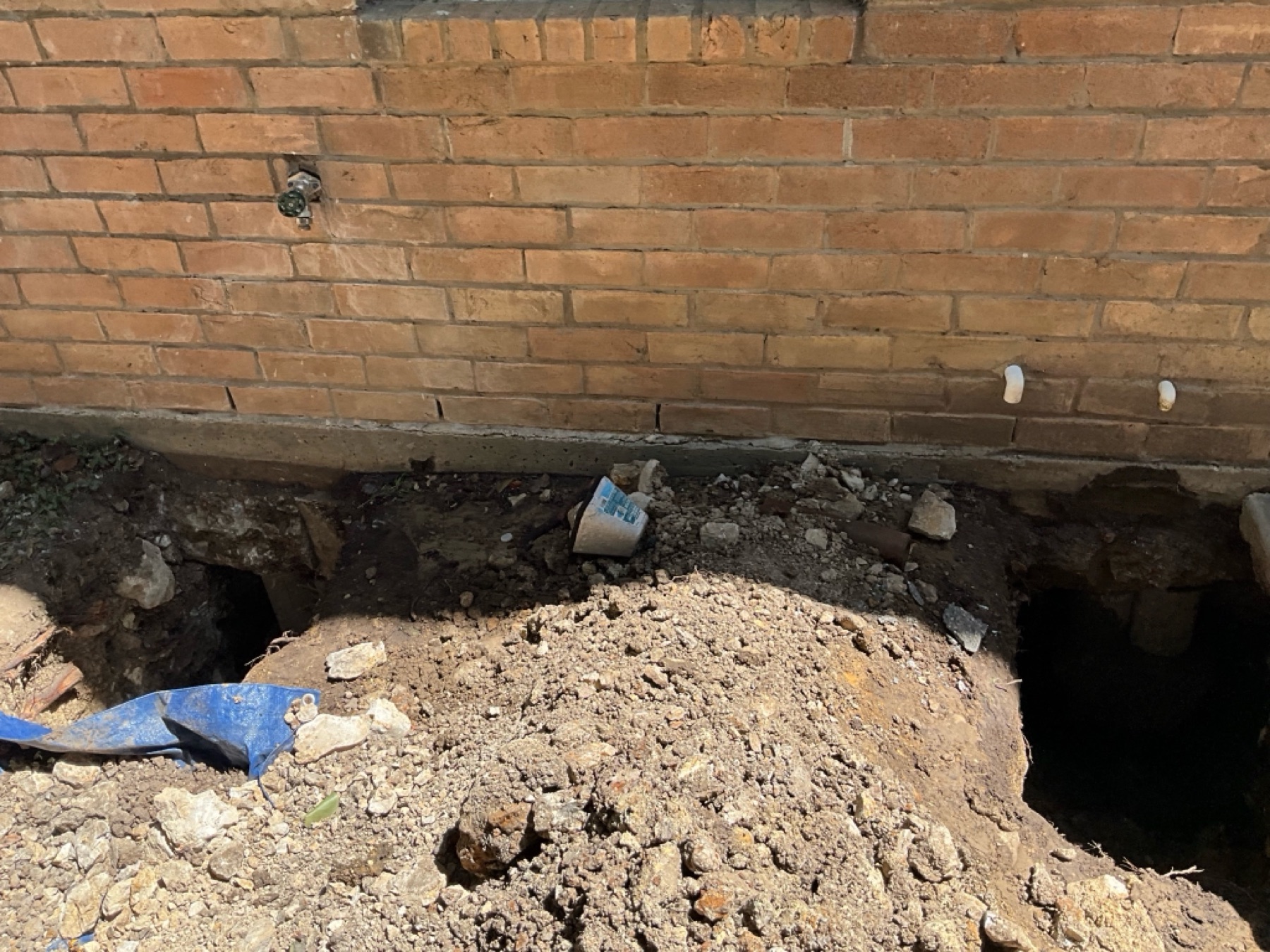 Hand excavation along the foundation wall — shovels and wheelbarrows only